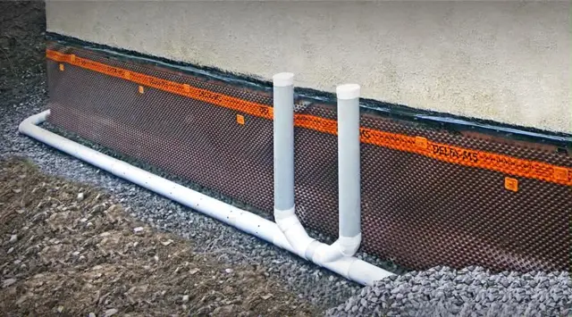Drain installé dans la pierre au pied d’une fondation protégée par une membrane